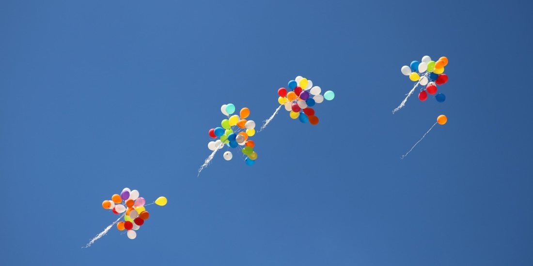 Mehrere Bündel bunter Ballons steigen in einen wolkenlosen Himmel auf