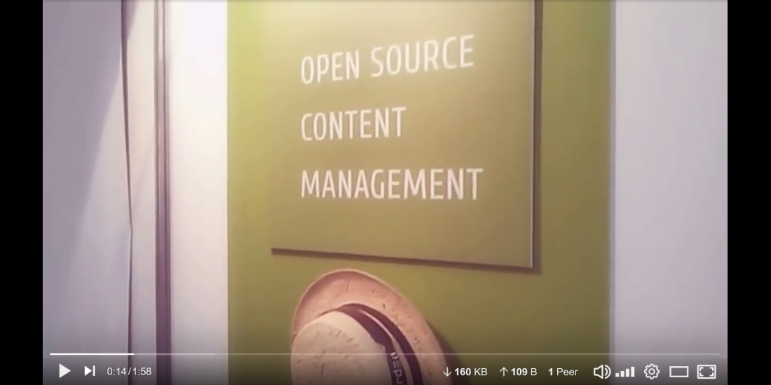 Still of a video: sign on a booth wall reading Open Source Content Management with a straw hat hanging below