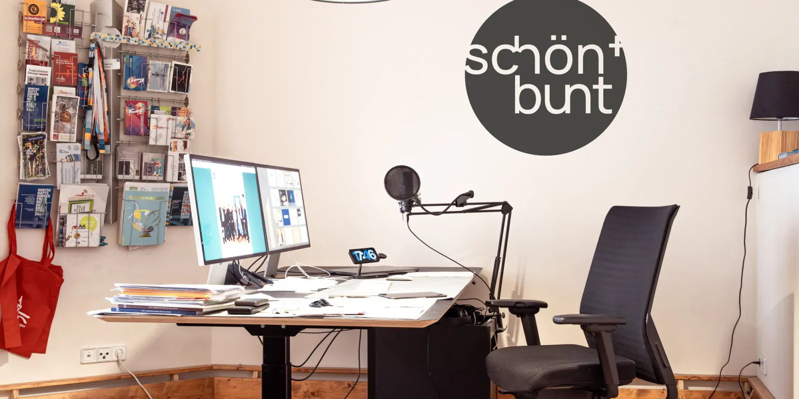 Blick in das Büro mit Schreibtisch, Bildschirmen, Bürostuhl, Flyerständer