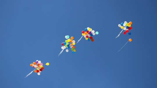 Several bundles of colorful balloons rising into a cloudless blue sky